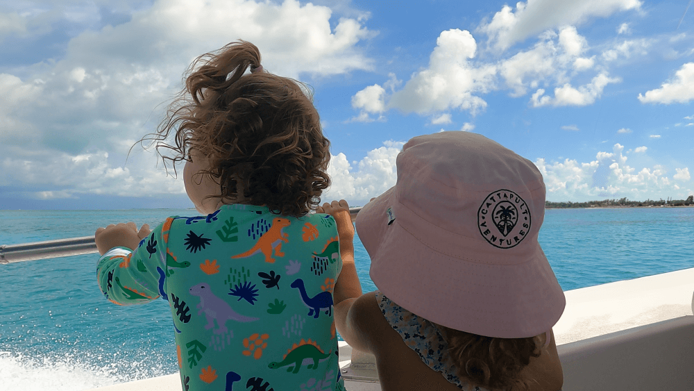2 children watching the sea from a boat, one wearing a Cattapult Ventures hat