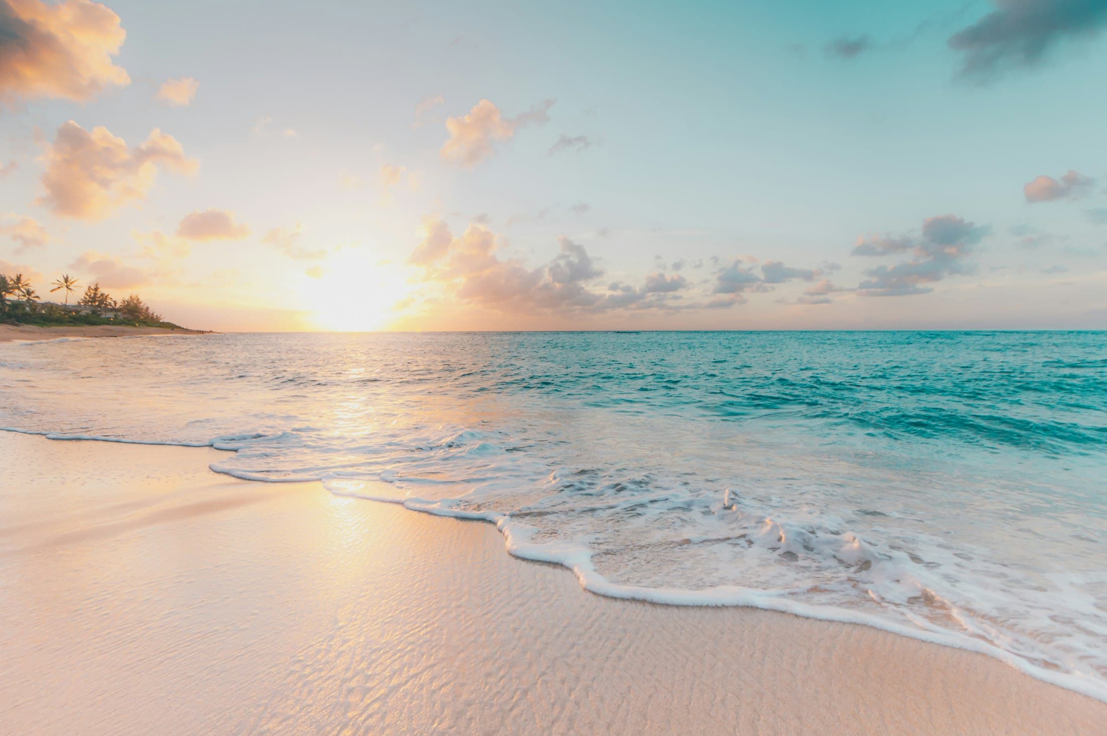 Sunrise over a calm turquoise sea and pale sand beach